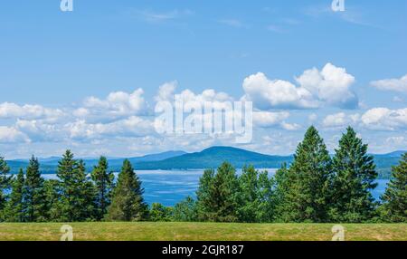 Malerischer Blick auf den Rangeley Lake, den bald Mountain und die weit entfernten Grate der Boundary Mountains, hinter einem Fichtenhain, unter bewölktem Himmel. Stockfoto