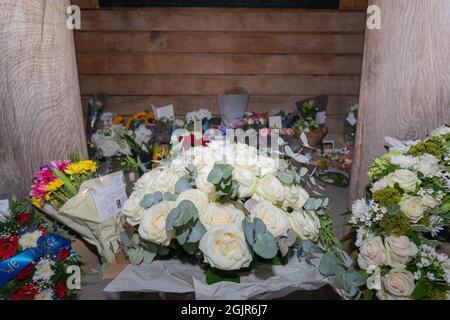 September 2021. London, Großbritannien. 11. September Gedenkfeier in Grosvenor Gardens, London. Ein zentraler Blumenstrauß aus weißen Rosen mit grünem Laub wird auf einem weißen Tuch platziert, umgeben von leuchtenden Blumenarrangements wie Sonnenblumen, rosa Rosen und gemischten Sträußen. Karten und Bänder begleiten die Blumen und vermitteln Erinnerungsbotschaften. Der Tribut wird von einer Holzwand und zwei großen Säulen eingerahmt, die eine feierliche und respektvolle Umgebung schaffen. Die Szene ruft Themen der transatlantischen Solidarität, der öffentlichen Trauer und der bürgerlichen Erinnerung hervor. Penelope Barritt/Alamy Live News Stockfoto