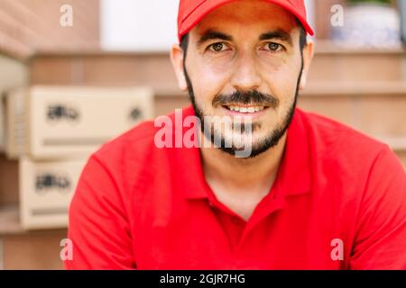 Porträt eines hispanischen Lieferers in roter Uniform mit Paketen im Hintergrund Stockfoto