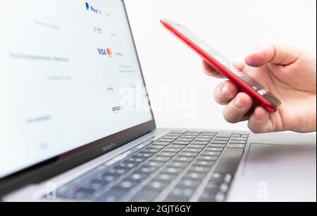 Rottweil, Deutschland. September 2021. Ein Mann hält sein Smartphone zur zwei-Faktor-Authentifizierung, während ein Laptop-Bildschirm verschiedene Zahlungsmethoden anzeigt. Kredit: Silas Stein/dpa/Alamy Live Nachrichten Stockfoto