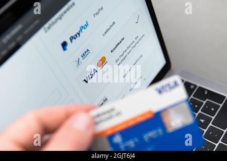 Rottweil, Deutschland. September 2021. Ein Mann hält seine Kreditkarte in der Hand, während verschiedene Zahlungsmethoden auf dem Bildschirm eines Laptops angezeigt werden. Kredit: Silas Stein/dpa/Alamy Live Nachrichten Stockfoto