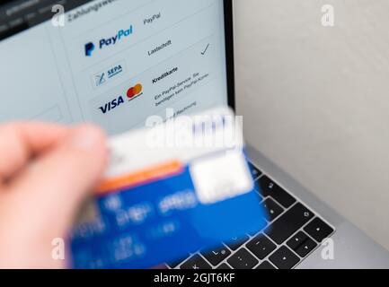 Rottweil, Deutschland. September 2021. Ein Mann hält seine Kreditkarte in der Hand, während verschiedene Zahlungsmethoden auf dem Bildschirm eines Laptops angezeigt werden. Kredit: Silas Stein/dpa/Alamy Live Nachrichten Stockfoto