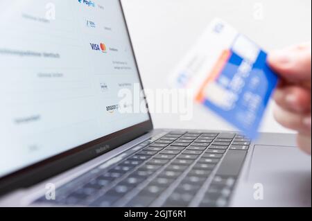 Rottweil, Deutschland. September 2021. Ein Mann hält seine Kreditkarte in der Hand, während verschiedene Zahlungsmethoden auf dem Bildschirm eines Laptops angezeigt werden. Kredit: Silas Stein/dpa/Alamy Live Nachrichten Stockfoto