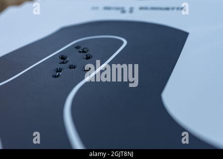 Nahaufnahme mit einer geringen Schärfentiefe eines schwarzen Papiersilhouettenziels, das mehrere Einschusslöcher im Kopfbereich des Ziels aufweist. Stockfoto