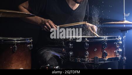 Ein männlicher Schlagzeuger spielt in einem dunklen Raum eine Snare-Trommel mit Drumsticks. Stockfoto