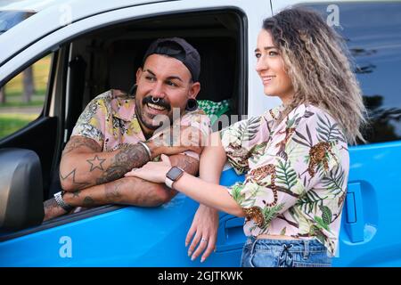 Das junge tätowierte Paar lächelte mit ihrem Van. Stockfoto