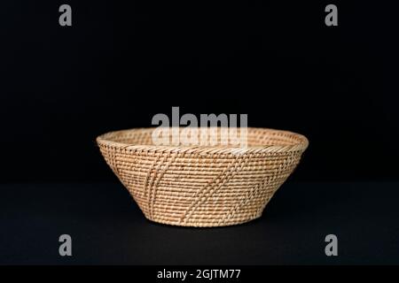 Eine schöne Rattanschale auf schwarzem Hintergrund. Stockfoto