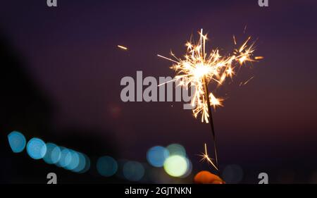 Hand hält einen Funkler am Strand während des Sonnenuntergangs mit Bokeh hellen Hintergrund. Konzept für Neujahr oder Weihnachtsfeier. Stockfoto