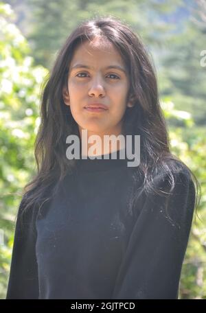 Nahaufnahme eines schönen indischen jungen Mädchens, das ein schwarzes Sweatshirt trägt und draußen in der Natur posiert, mit Blick auf die Kamera Stockfoto