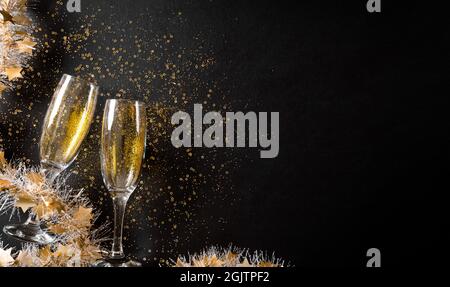 Weihnachts- und Neujahrsferien-Hintergrundkonzept aus Sektgläsern mit goldenem Glitzer auf schwarzem Holzhintergrund. Stockfoto