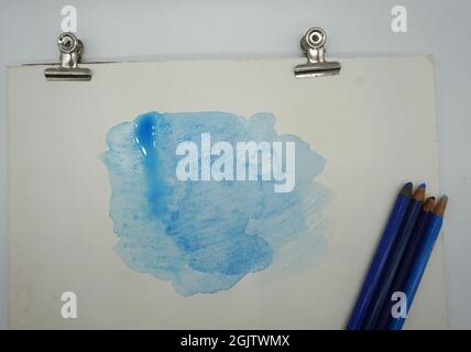 Blaue Buntstifte und Marker, Farben und Wasser lösen sich in Aquarelle auf. Stockfoto