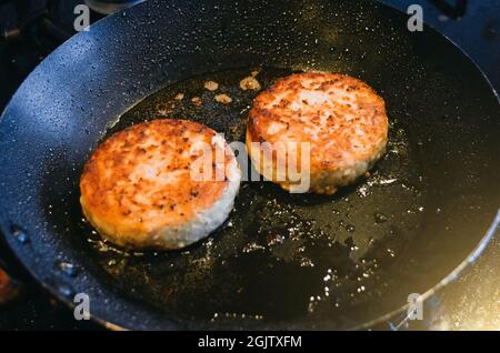 Zwei runde Koteletts aus Rindfleisch werden darin gebraten Eine Pfanne und Öl Stockfoto