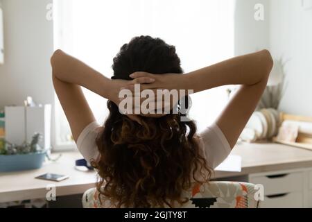 Frau, die sich auf dem Stuhl mit den Händen hinter dem Kopf entspannt, Rückansicht Stockfoto