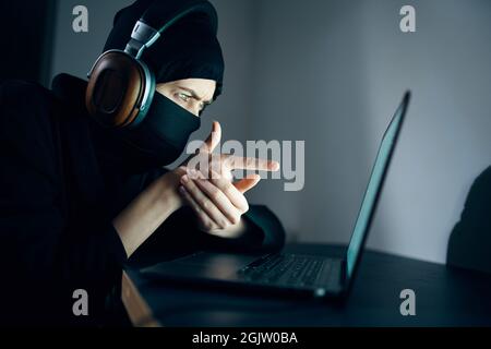 Frau in Maske vor Laptop-Kopfhörer-Hacking Stockfoto