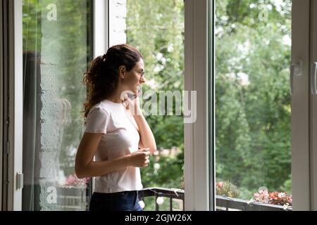 Eine Frau spricht mit einem Freund am Handy, der in der Nähe eines offenen Fensters steht Stockfoto