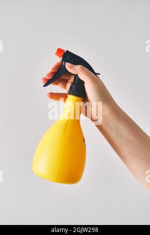 Eine junge Frau hält eine Sprühflasche in der Hand. Gelbe Sprühflasche auf weißem Hintergrund Stockfoto