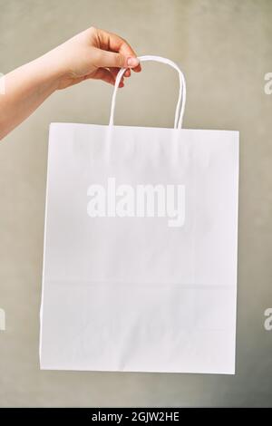 Junge Frau hält weiße Papiereinwegtasche in der Hand auf grauem Hintergrund Stockfoto