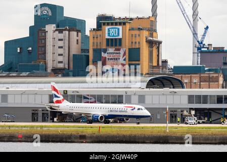 London City Airport, mit der legendären Zuckerfabrik Tate & Lyle im Hintergrund. British Airways CityFlyer Embraer ERJ 190 Jet-Linienflugzeug auf Stand Stockfoto