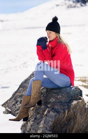 Blonde Frau, die im Winter auf einem Felsen in den verschneiten Bergen in der Sierra Nevada, Granada, Spanien, sitzt. Stockfoto