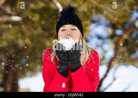 Blonde Frau, die im Winter einen Schneeball bläst, in der Sierra Nevada, Granada, Spanien. Stockfoto