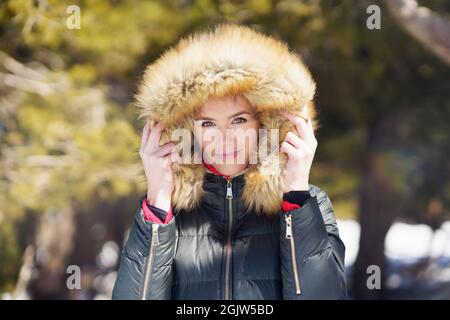 Junge Frau in einer pelzigen Kapuzenjacke, die im Winter die verschneiten Berge genießt. Stockfoto