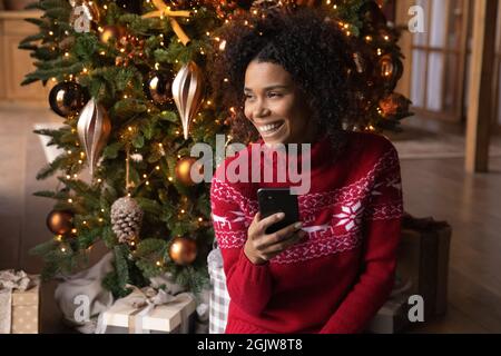 Lächelnde Biracial Frau verwenden Handy in der Nähe von Weihnachtsbaum Stockfoto