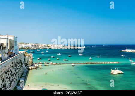 Panoramablick auf die Meereslandschaft von Otranto von der Bastion der Burg aus gesehen, mit festfahrenden Booten, Badegäste und Sonnenschirmen, in Otranto, Salento, Italien Stockfoto