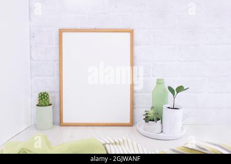 Leeres Bild-Mockup mit Holzrahmen auf weißem Backstein Wand Hintergrund mit Sukkulenten Pflanzen und grüne Vase. Heller Innenraum Stockfoto