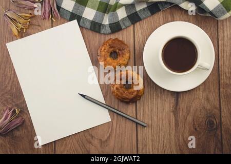 Leeres Papier mit Bleistift, eine Tasse Kaffee mit Cupcakes, getrockneten Blumen und eine Decke auf einem Holzboden. Schreibwaren, Draufsicht Stockfoto