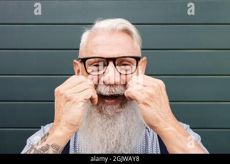 Glücklicher Hipster Senior lächelt vor der Kamera in der Stadt - Fokus auf Gesicht Stockfoto