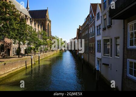 Blick auf den typisch holländischen Wasserkanal mit gotischer Kirchenfassade und Wohnhäusern gegen den blauen Sommerhimmel - Dordrecht, Niederlande Stockfoto