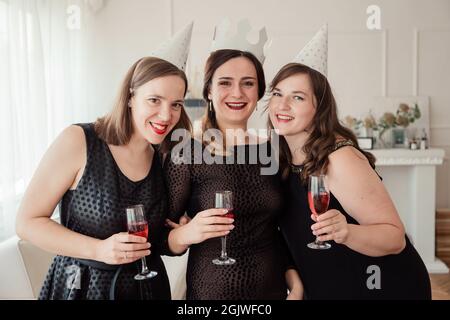 Frauenparty. Freundinnen Mädchen in schwarzen Kleidern küssen das Geburtstagskind. Gläser mit rosa Champagner in den Händen. Stockfoto