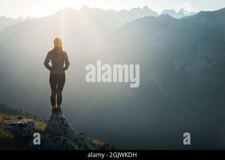 Junge Wanderin, die bei Sonnenaufgang am Rand der Klippe steht. Weibliche Touristen erreichen Gipfel genießen erstaunliche Sonnenaufgang in den Bergen.Backlight sunligh Stockfoto