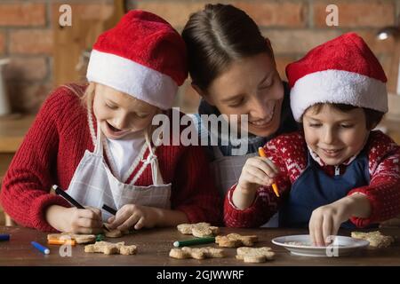 Junge Mutter, die mit kleinen Kindern WeihnachtsLebkuchen dekorierte. Stockfoto