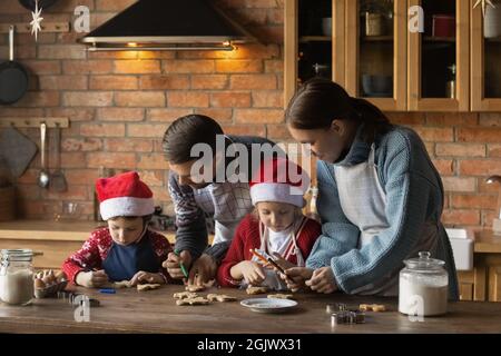 Glückliche Familie mit kleinen Kindern, die Weihnachtskekse dekorieren. Stockfoto