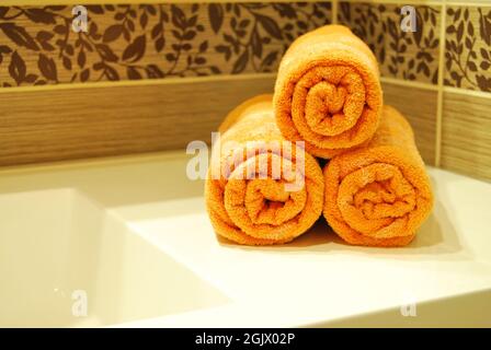 Drei orangefarbene Handtücher auf einem Keramikwaschbecken in einem luxuriösen und sauberen Badezimmer Stockfoto