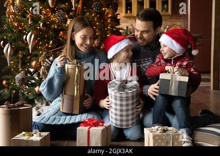 Lächelndes junges Familienpaar, das Weihnachtsgeschenke mit Kindern auspacken kann. Stockfoto