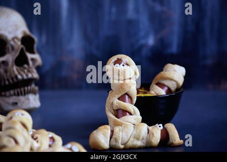 Tolles Essen für Kinder. Mama Hot Dogs auf einem blauen rustikalen Tisch mit einer Schüssel Ketchup und Senf Dip, mit Spinnennetz-Design. Stockfoto