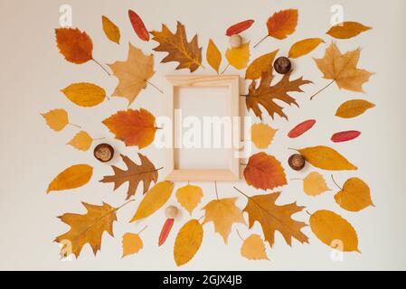 Herbstliche Blätter, die nebeneinander um einen Holzrahmen auf beigem Hintergrund angeordnet sind. Speicherplatz Kopieren Stockfoto