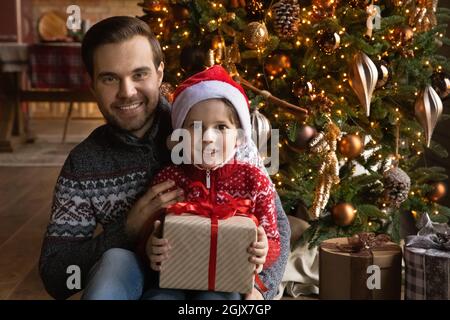 Porträt eines glücklichen jungen Vaters mit Sohn, der Weihnachtsgeschenk hält. Stockfoto