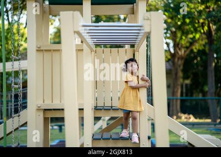 Ein süßes thailändisches Kind in gelbem Kleid, das auf dem Spielplatz im Park spielt Stockfoto