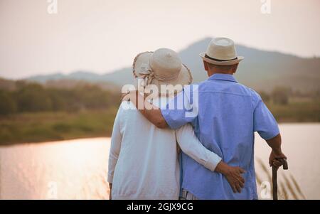 Liebe und Valentinstag Konzept. Ein glückliches Seniorenpaar, das während des Sonnenuntergangs in der Nähe von Berg und See steht, Senior Healthcare und Relationship. Stockfoto