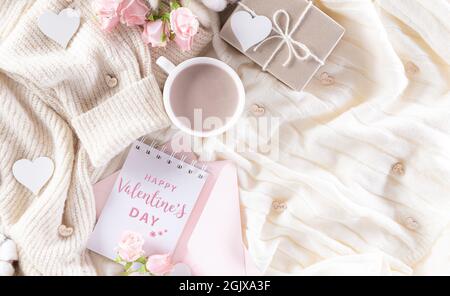 Liebe und Valentinstag-Konzept, Herzen mit Geschenkbox und Rosen, Kaffeetasse auf beigem Pullover oder cremefarbener Strickdecke und flauschiger Hintergrund. Stockfoto