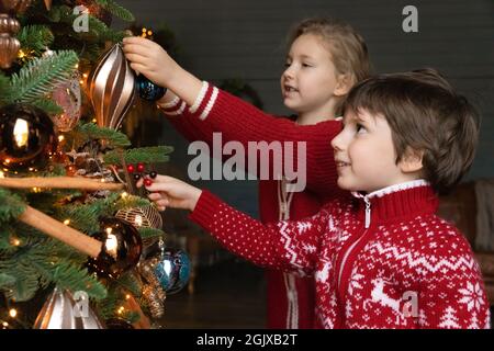 Glücklich aufgeregt kleine Kinder schmücken Weihnachtsbaum mit Kugeln. Stockfoto