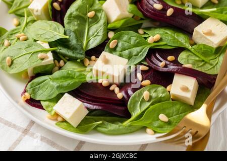 Gerösteter Rübensalat mit gewürfeltem Feta-Käse, Pinienkernen und Spinat auf einem weißen Teller mit goldenem Besteck auf einem Holztisch, kanadische Küche, Nahaufnahme Stockfoto