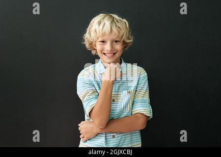 Porträt eines glücklichen lächelnden kaukasischen Jungen, der auf einem schwarzen Brett auf dem Hintergrund steht. Stockfoto