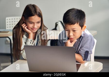 Zwei verschiedene Schüler sehen sich gemeinsam Lernvideos auf einem Laptop an. Stockfoto