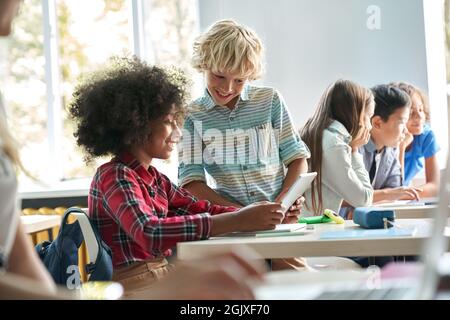 Afroamerikanisches Mädchen und kaukasischer Junge Schulkinder arbeiten im Klassenzimmer zusammen. Stockfoto