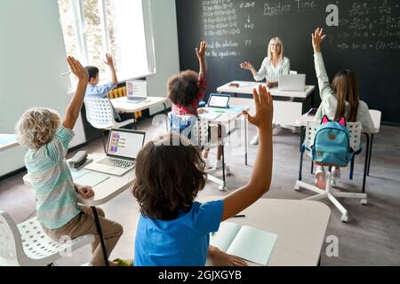 Lächelnder, fröhlicher Lehrer, der Matheunterricht mit Schulkindern am Schreibtisch hatte. Stockfoto