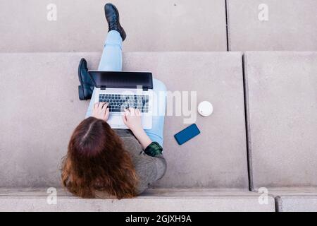 Porträt einer freiberuflichen Frau, die einen Laptop benutzt, während sie auf einer Treppe in der Stadtstraße sitzt. Blogger-Konzept. Stockfoto